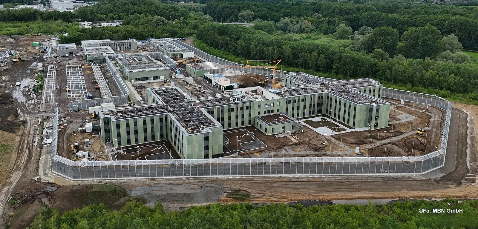 Luftaufnahme der im Bau befindlichen forensischen Klinik in Lünen mit mehreren Baukörpern hinter einer Sicherheitsumzäunung
