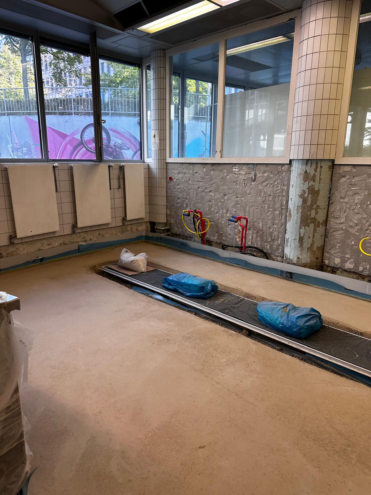 Eingebaute Entwässerungsrinne in einer Bodenaussparung, die umgebende Fläche ist vorbereitet, an der Wand liegen Anschlussleitungen frei